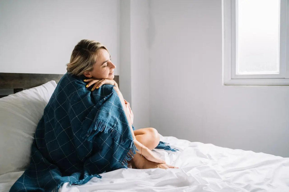 A woman in a blue blanket sitting in the corner of her bed