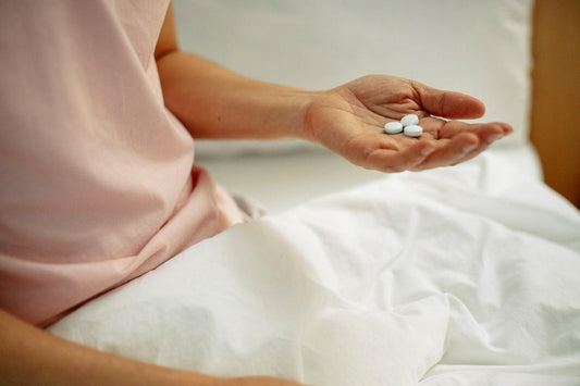 A person sitting under a blanket with painkillers in their hand